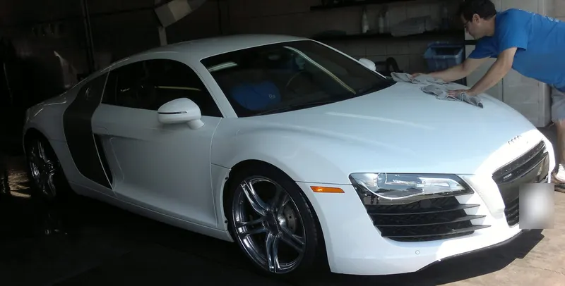 Detailer in a blue shirt hand-drying the hood of a white Audi R8 with a microfiber towel in the wash bay